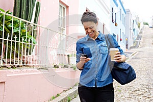 Smiling young woman walking with mobile phone and bag