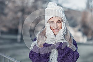 Smiling young woman in warm clothing on winter day outdoors. Happy girl wearing wool cap, scarf and sweater. Snow people concept