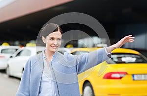 Smiling young woman waving hand and catching taxi