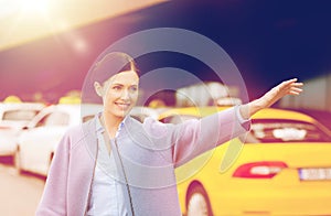 Smiling young woman waving hand and catching taxi