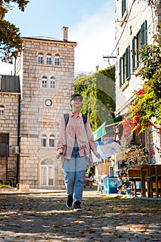 Smiling young woman wearing cap and sunglasses walks through old city. Vertical orientation. Tower in background. Summer