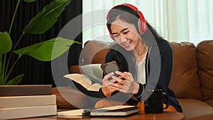 Smiling young woman wearing headphone and chatting online, typing text message on smart phone