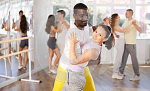 Smiling young woman wearing sportswear dancing in couple samba dance with african american partner during group class at