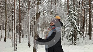 Smiling young woman wearing warm clothes shaking tree and getting covered in snow in winter forest