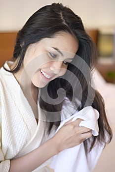 Smiling young woman wearing white bathrobe wiping her hair with towel after a shower in bedroom