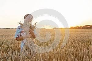 Smiling young woman in a wheat field at sunset with a bouquet of ears of corn in her hands