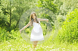 Smiling young woman in white dress against background of summer green park. Beautiful healthy happy girl enjoying freedom outside