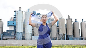 Smiling young woman worker posing with Argentina flag in hands against background of factory
