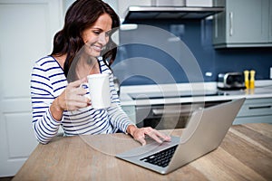 Smiling young woman working on laptop while holding coffee mug