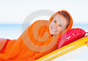 Smiling young woman wrapped in towel laying on sunbed