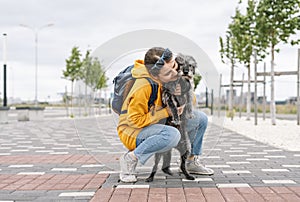 Smiling young woman in yellow hoodie hugging her fluffy shaggy gray dog, pet love and walking dog