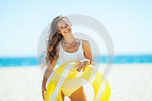 Smiling young woman with yellow inflatable lifebuoy on beach