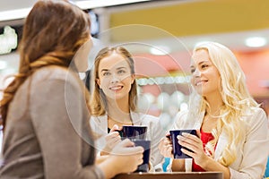 Smiling young women with cups in mall or cafe