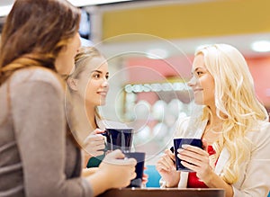 Smiling young women with cups in mall or cafe