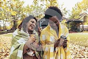 Smiling young women friends chatting outdoors and drink coffee while enjoying walk in park together