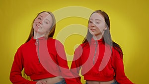 Smiling young women moving simultaneously dancing at yellow background looking at camera. Confident Caucasian twin