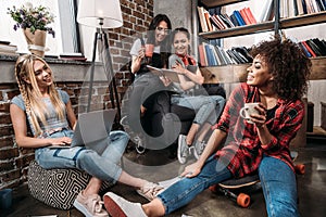 Smiling young women sitting together with laptop and coffee cups