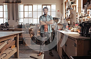 Smiling young woodworker standing in his workshop full of tools photo