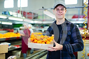Smiling young worker with box of mandarins at sorting line