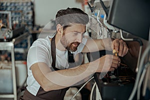 Smiling young worker repairing coffee machine in a workshop