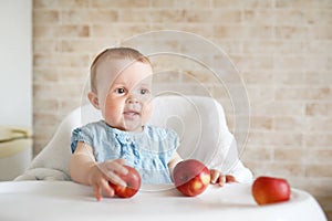 Baby eating fruit. Little girl biting yellow apple sitting in white high chair in sunny kitchen. Healthy nutrition for kids. Solid