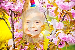Smilling blonde kid standing in a blooming garden. Blooming cherry. Portrait of beautiful little girl. Close up of