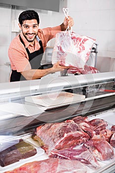 Smilling butcher is offering meat to clients in market.