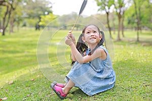 Smilling little Asian girl holding blank heart label lying on green grass at summer garden