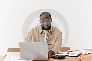 Smilling young afro american man counting expenses and keeping records on laptop, paper bank accounts are on the table