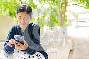 Smilng Asian woman using a mobile phone sitting on the chair at garden home outdoor