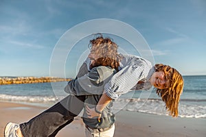 Smilng couple in love fool around while walking along the beach on sunny windy day