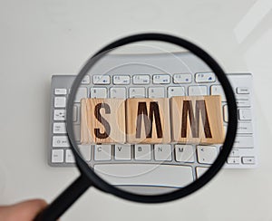 SMM abbreviation from wooden cubes on computer keyboard and magnifier