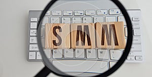 SMM abbreviation from wooden cubes on computer keyboard and magnifier