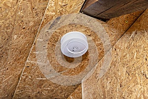 Smoke and carbon monoxide detector with a central LED, mounted on a ceiling lined with OSB boards.