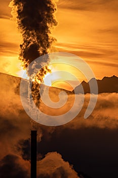 Smoke from chimny and colorful sky with sun and mountains at background