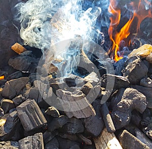 Smoke of the coal on the embers. Preparation of fire for barbecue embers. Outdoor recreation. Flames seen in the image