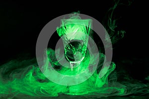 Smoke into cocktail glass on a black background. Witch potion background for Halloween. Unusual bar drink.