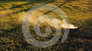 Smoke curl over sunlit green field