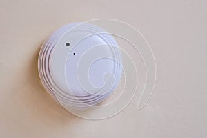 Smoke detector of fire alarm, the white background of the wall. Sensor on beige ceiling. Smoke fire alarm in the inactive state