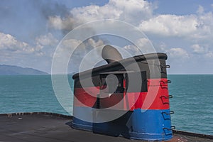 Smoke from ferry boat flue during sea with sunlight, sea water and blue sky in background, Thailand