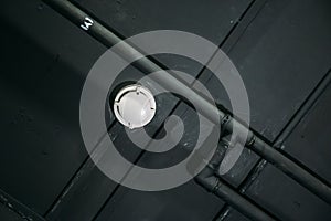 Smoke or fire detector on black celling with pipes
