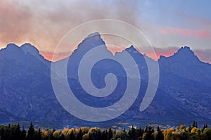 Smoke floats over a jagged mountain just before sunset.