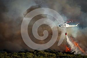 Smoke and huge fire and blurred helicopter with bambi bucket dumping water