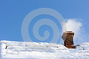 Smoke out of a brick chimney on a snowy rooftop