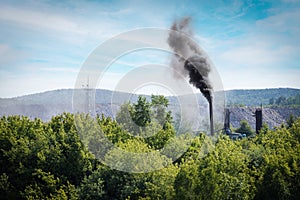 Smoke plume from industry emitting into the atmosphere on forest trees background and blue sky.