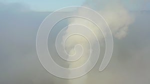 Smoke from a power station chimney rising from a low, creeping fog. Drone view