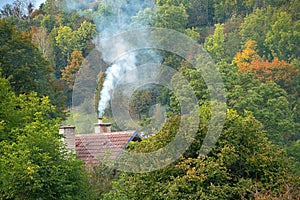 Smoke rises from the chimney on the house. Heating season. Roof with smoking chimney and trees in autumn
