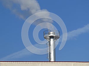 Smoke spews out of a chimney on the roof at an industrial plant photo