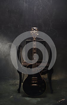 Smoke swirls out of moody lit stillife of black electric guitar and amp