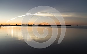 Smoke trail from a rocket at sunset with reflection in water